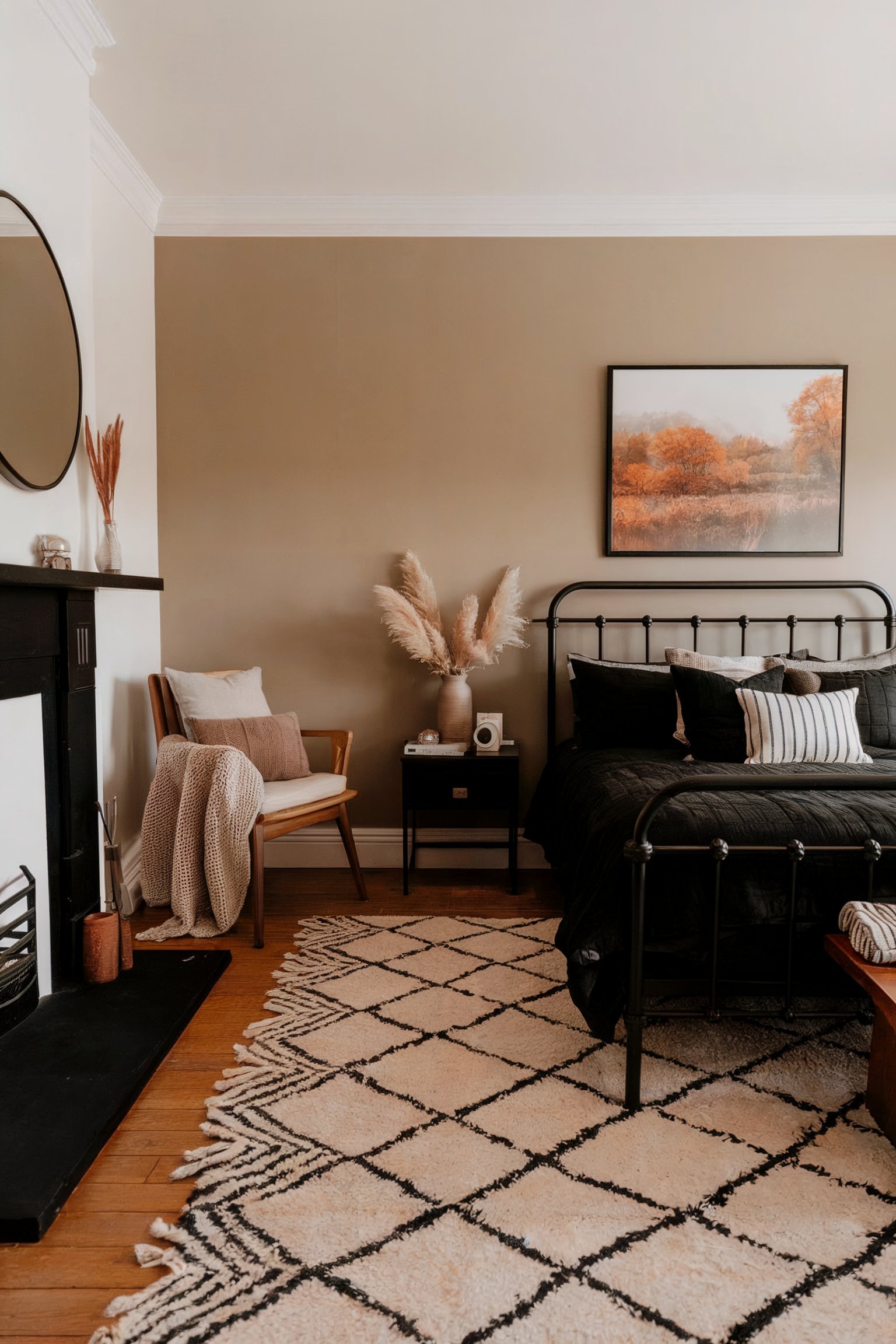 A neutral-toned bedroom with a black metal bed frame, pampas grass in a vase, and a landscape painting on the wall