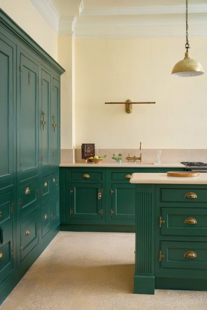 Kitchen with green cabinets, brass accents, cream walls, beige countertops, and minimalist lighting.