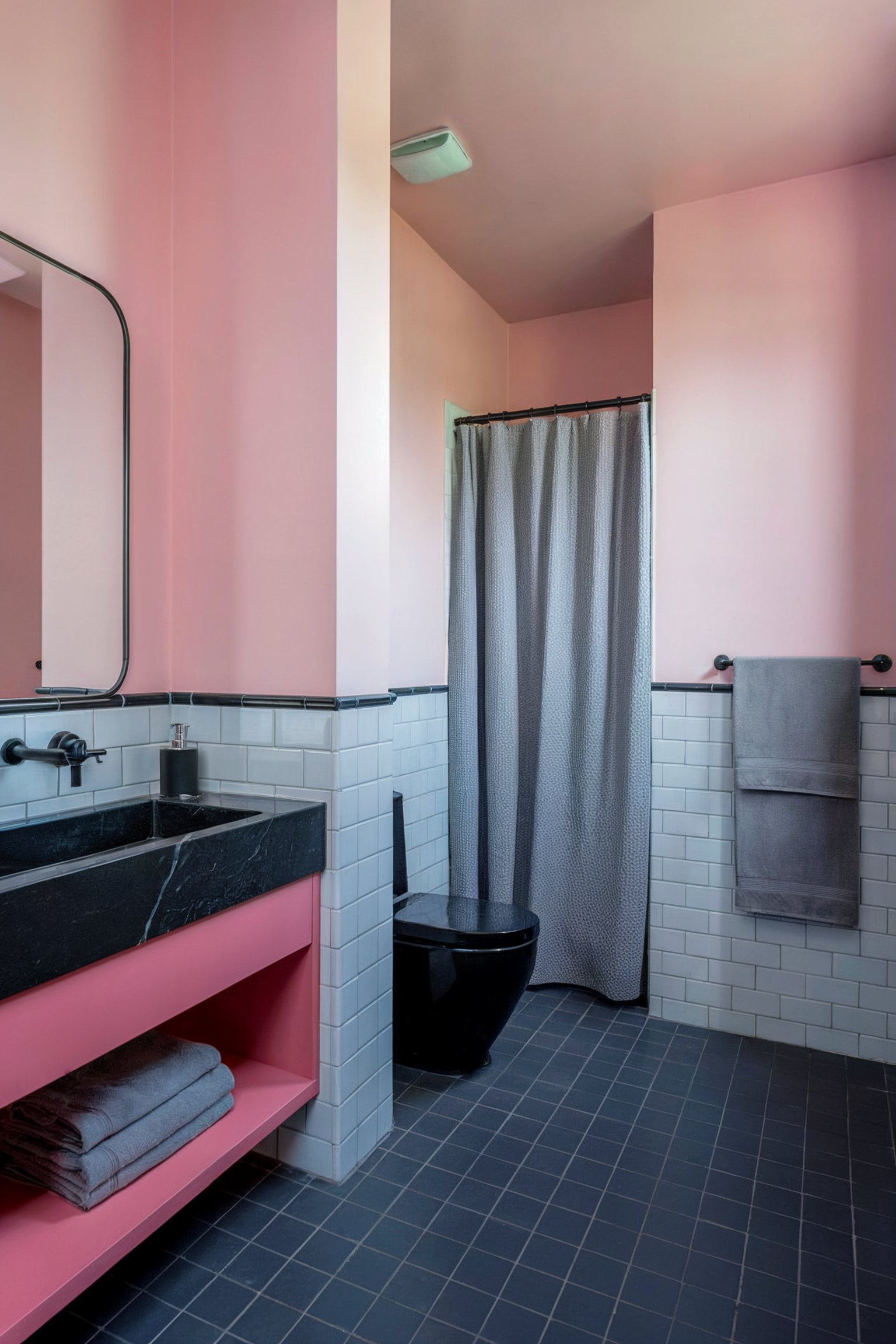 Minimalist pink and gray bathroom featuring a black vanity, black toilet, and a tiled shower, with a modern industrial feel