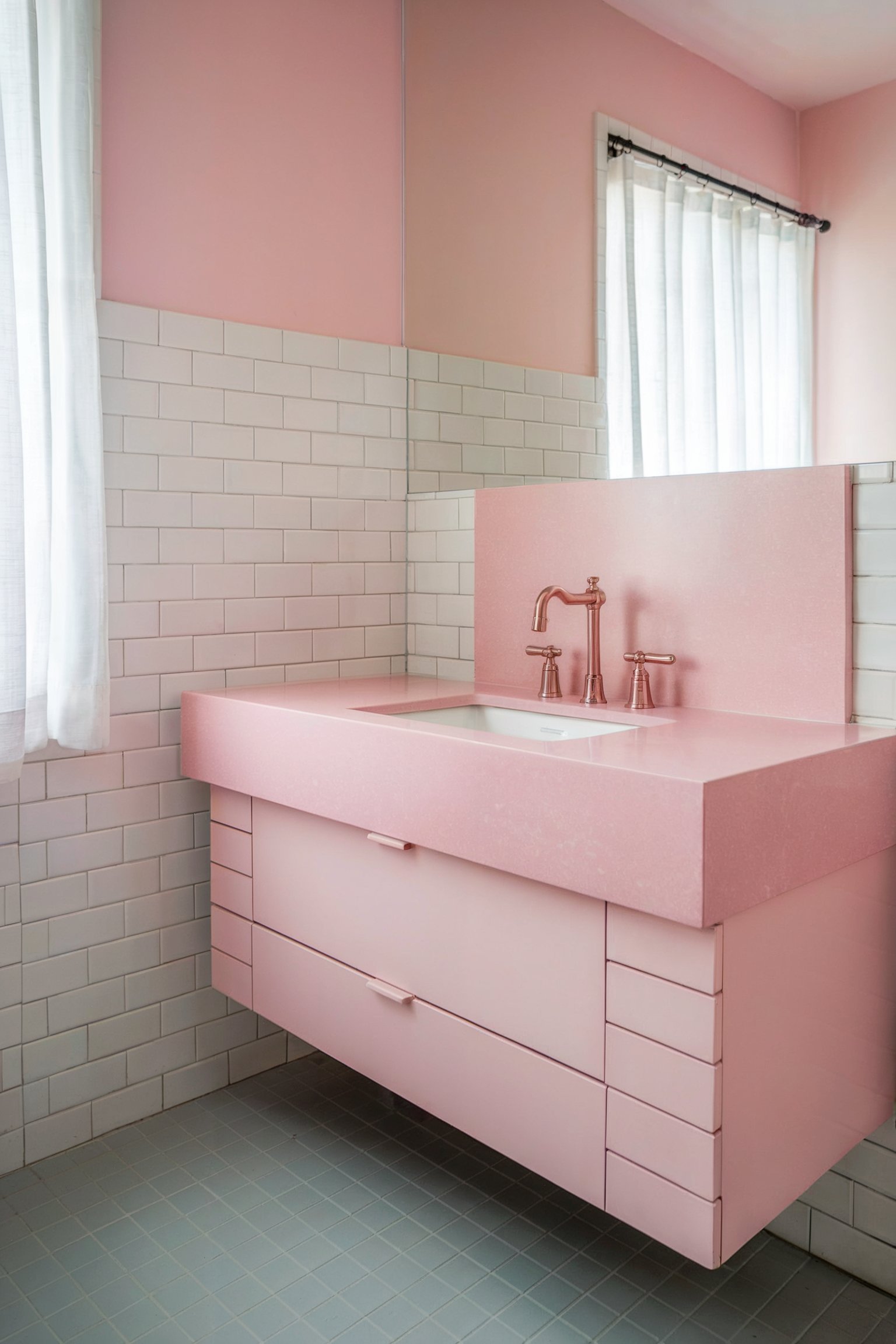 A sleek pink bathroom vanity with pink countertops and rose gold fixtures against white subway tile walls