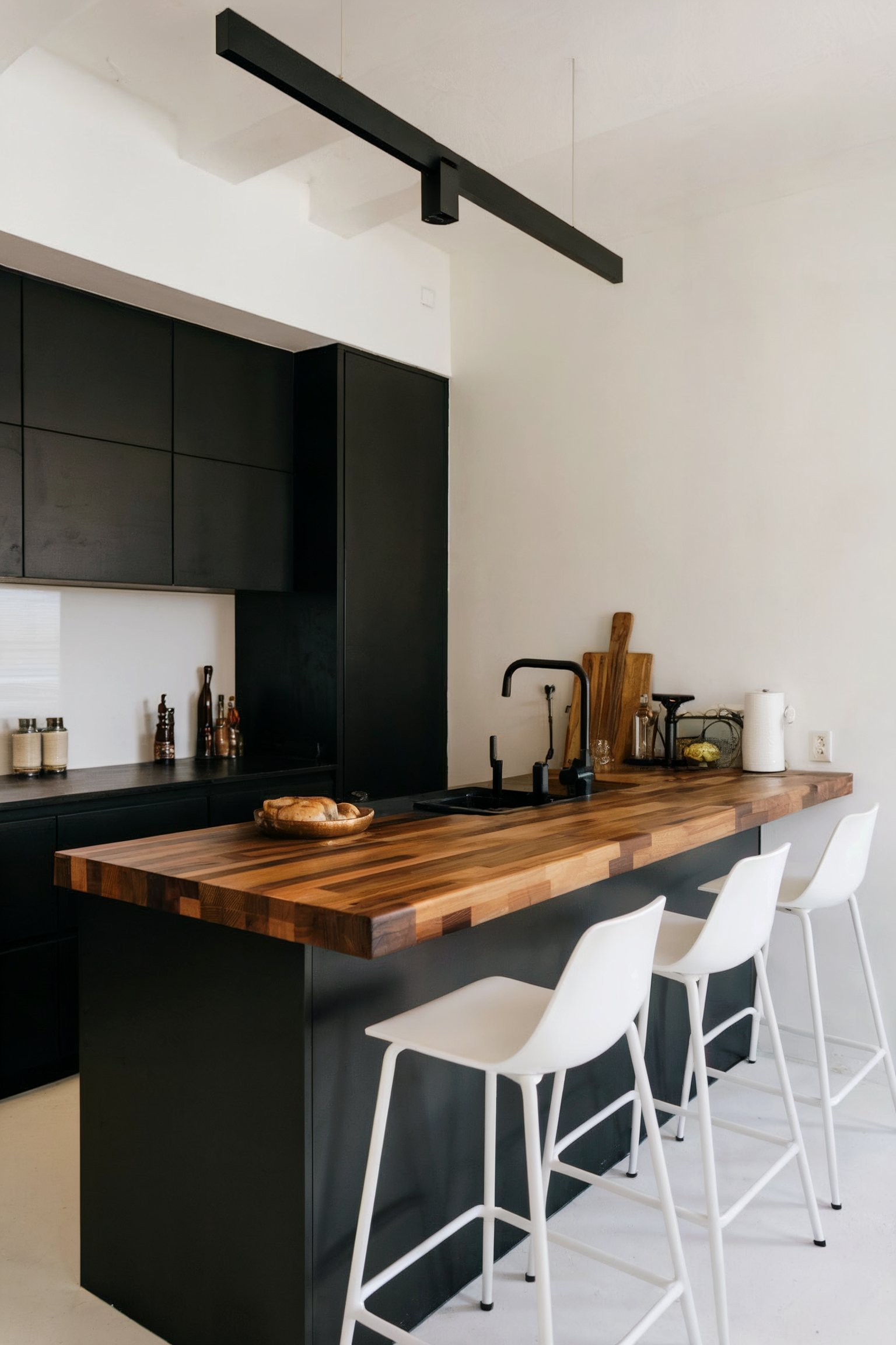 A modern black kitchen with a wooden butcher block countertop, white walls, and minimalist black cabinetry