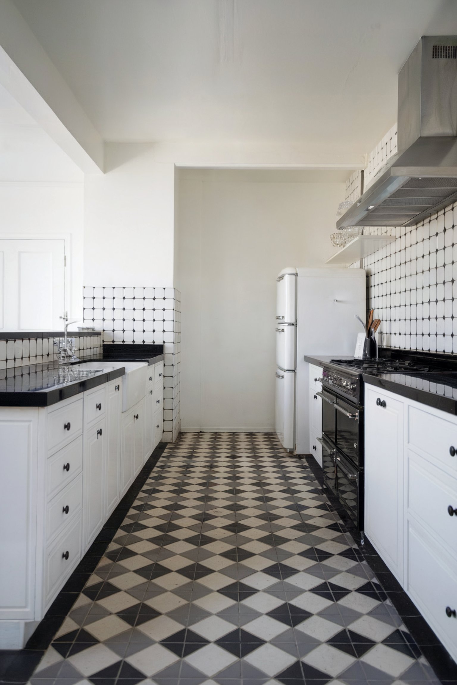 A long, narrow kitchen with black and white checkered flooring, white cabinets, and a vintage-style black stove