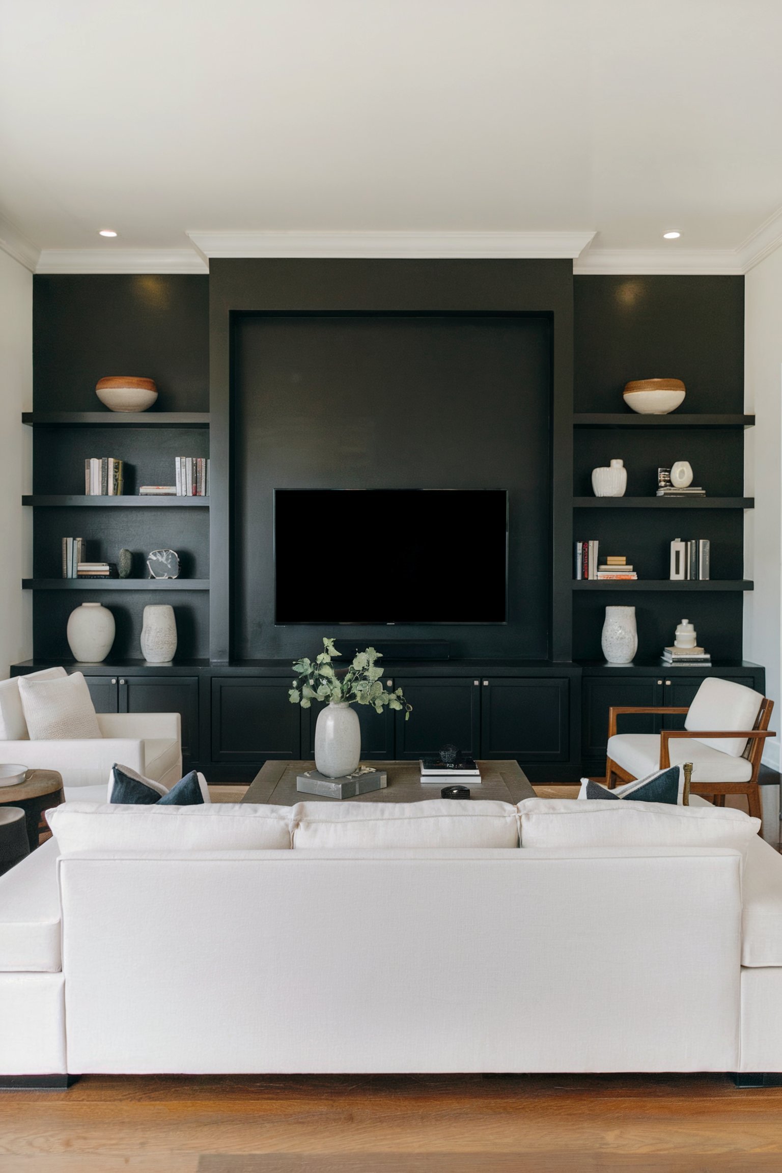A modern living room with a black accent wall featuring built-in shelves around a TV, paired with light furniture for a striking contrast