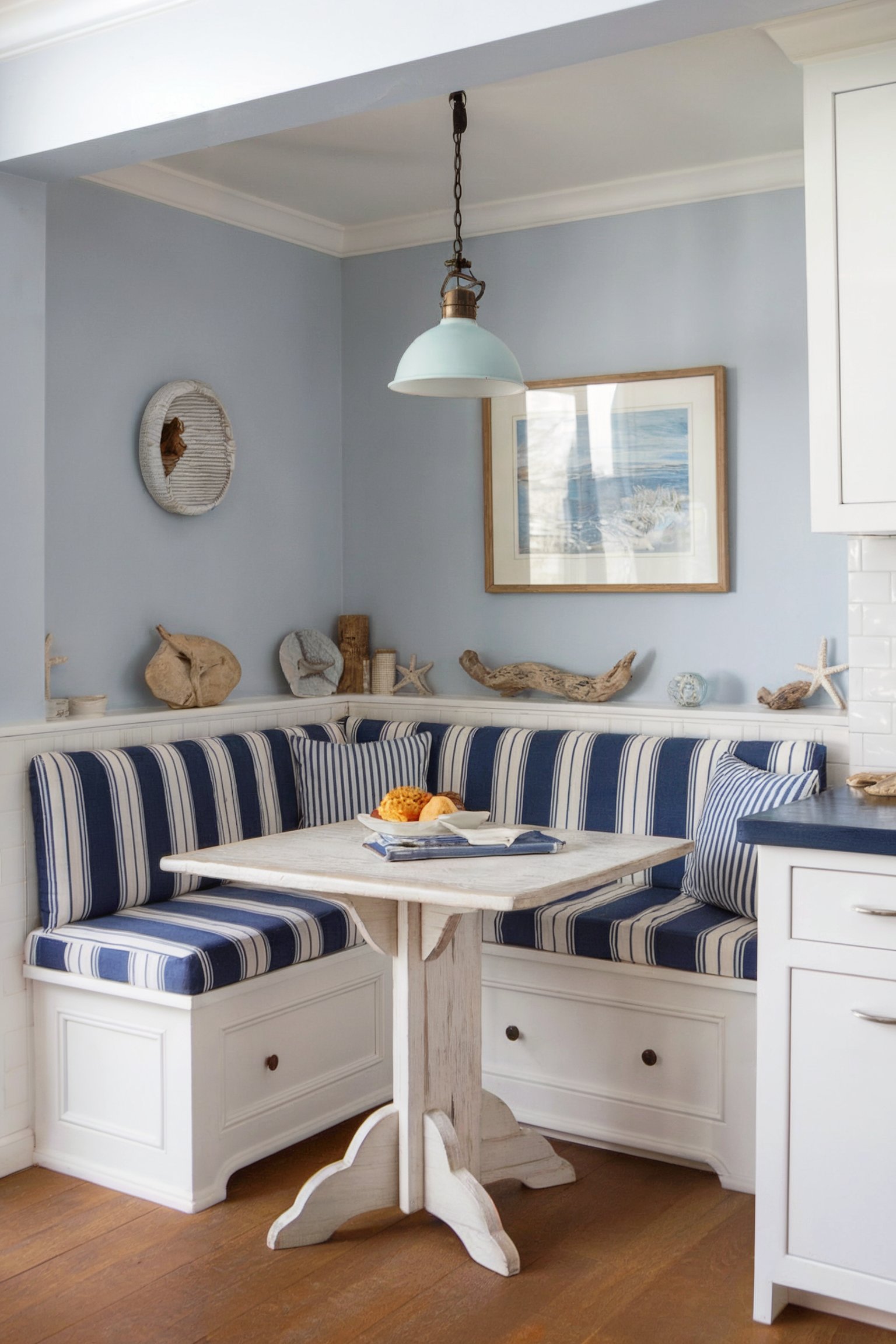 A cozy kitchen nook with a coastal theme featuring blue striped cushions, a white table, and ocean-inspired decor