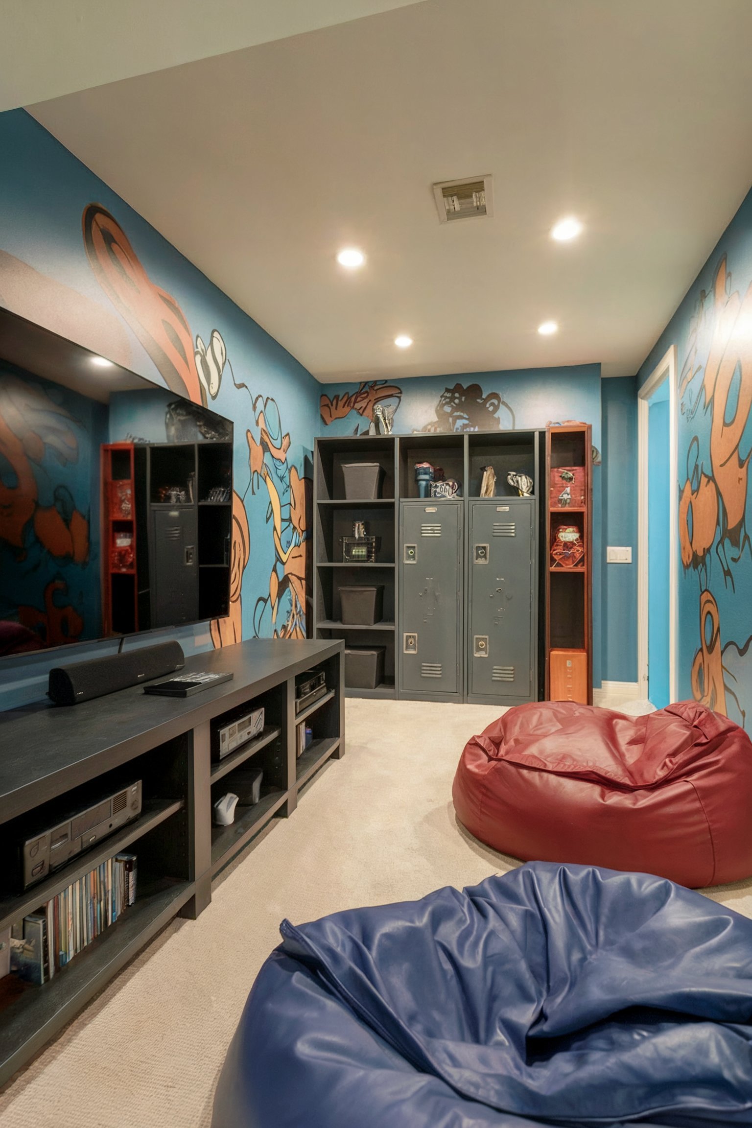 A basement room designed as a teen's lounge with vibrant graffiti-style wall art, bean bag chairs, lockers, and a TV setup