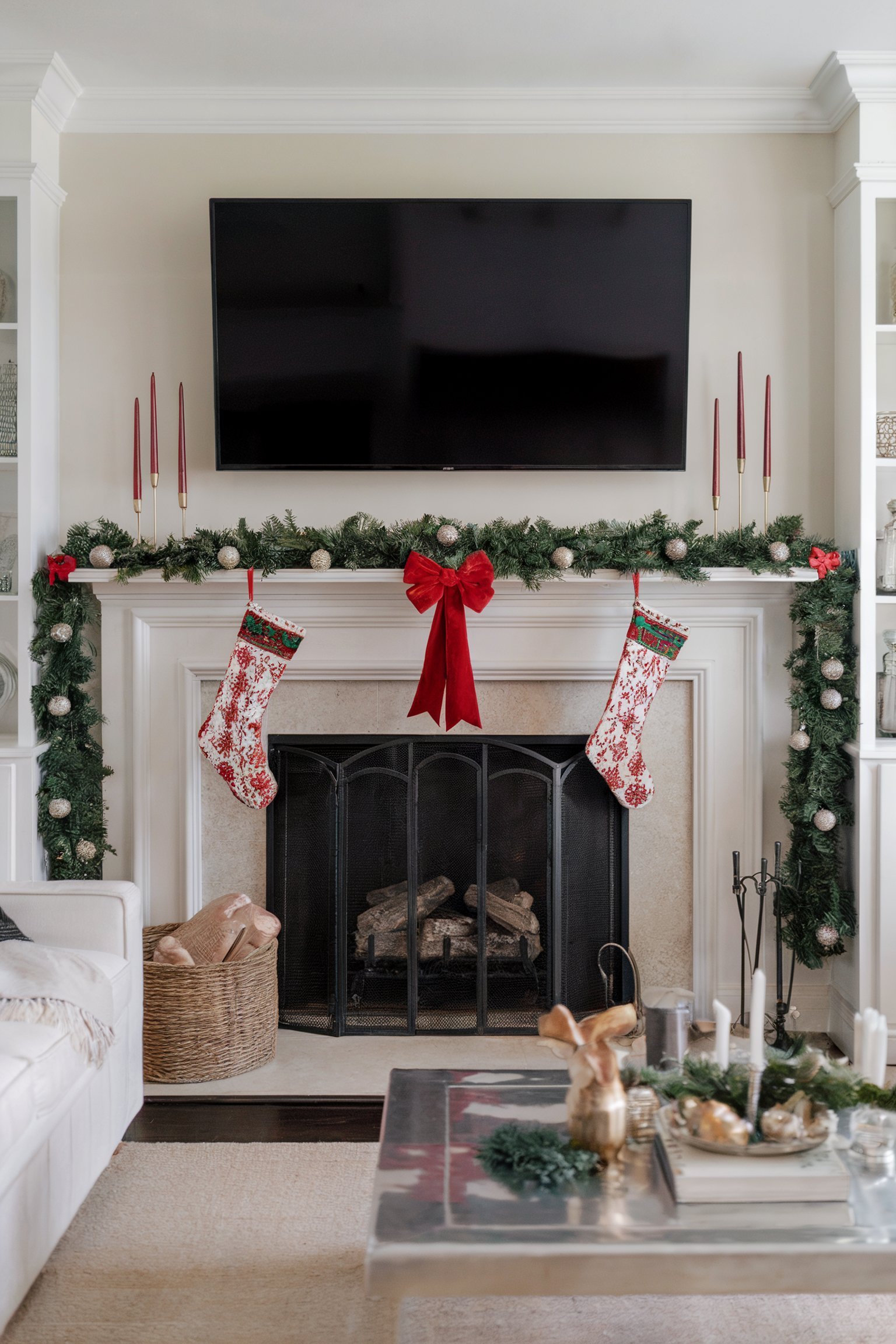 White fireplace with TV above, decorated with a garland, red bows, red taper candles, and red-and-white stockings