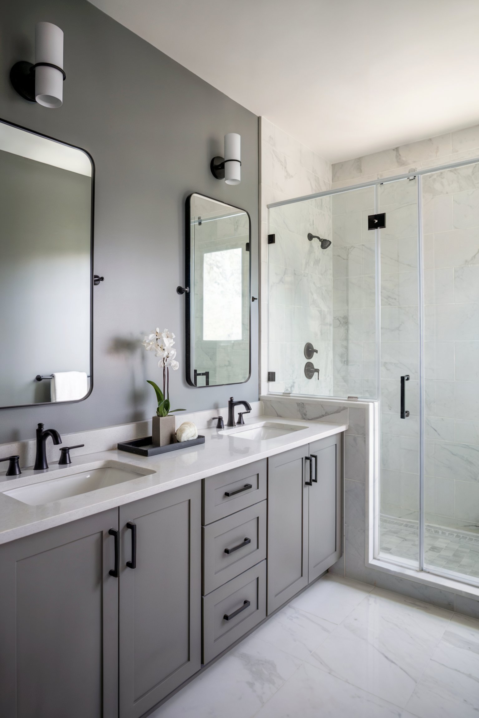 A modern bathroom with light gray cabinetry, a double sink, and a glass shower