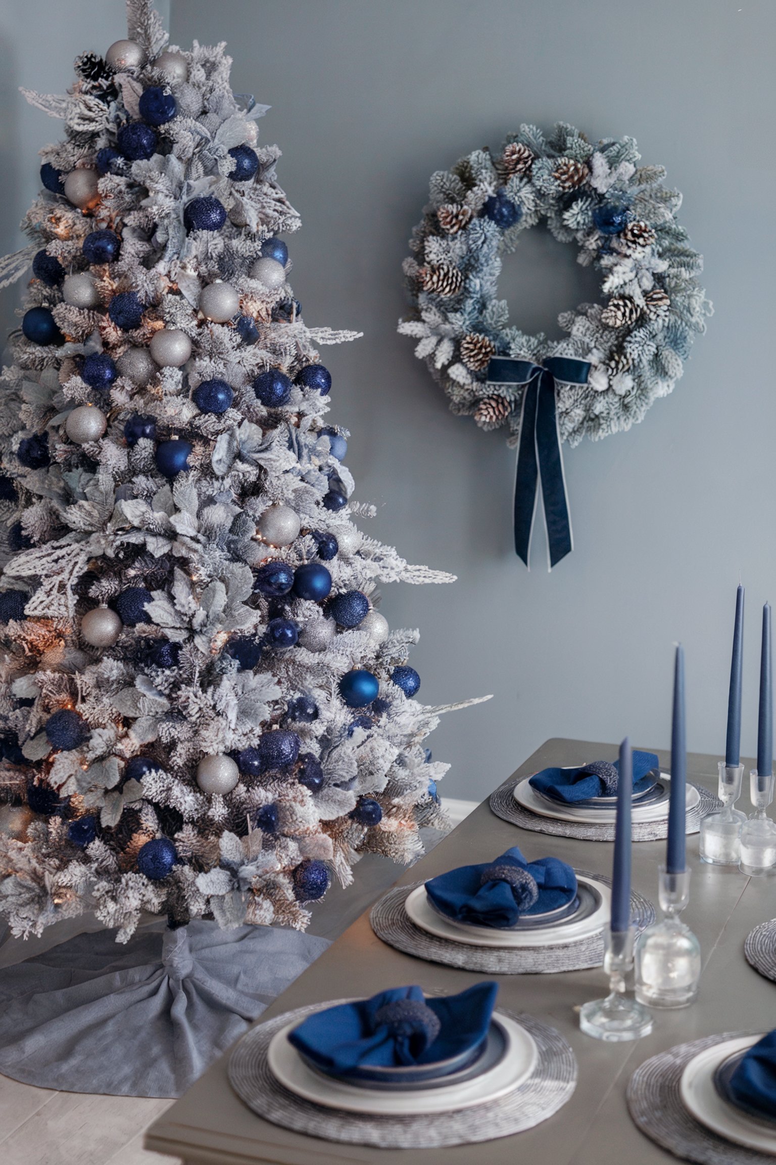 Snowy tree with blue and silver ornaments beside a matching wreath, and blue table setting