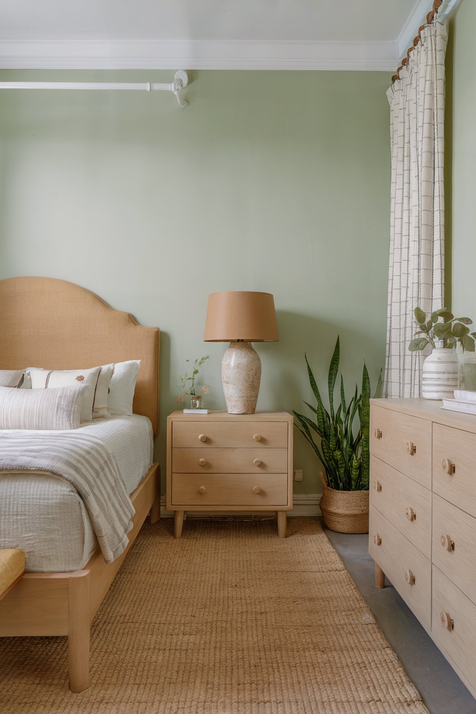 Light green bedroom with a tan bed, wood furniture, and a woven rug