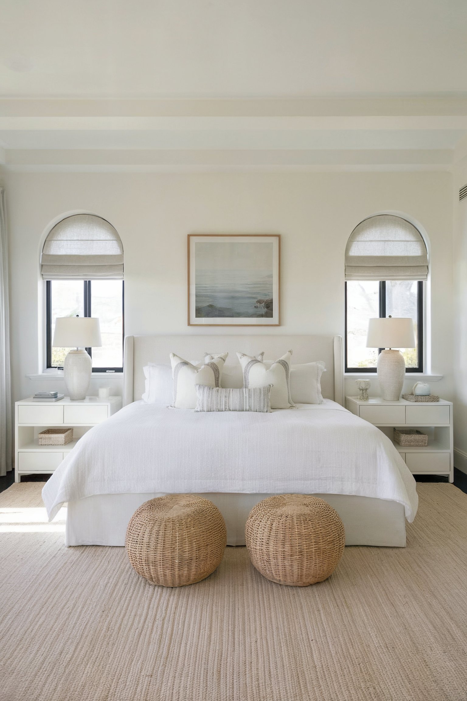 Neutral coastal bedroom decor with a white bed, wicker cushions, and an ocean painting