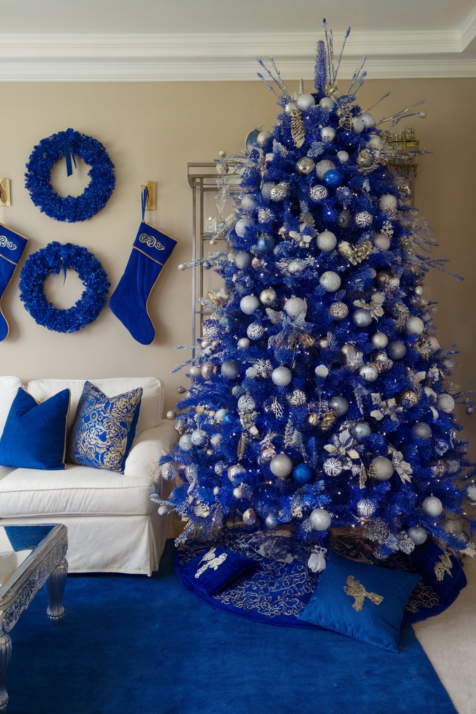 A living room with a bright blue Christmas tree decorated with silver and blue ornaments, matching wreaths and stockings on the wall