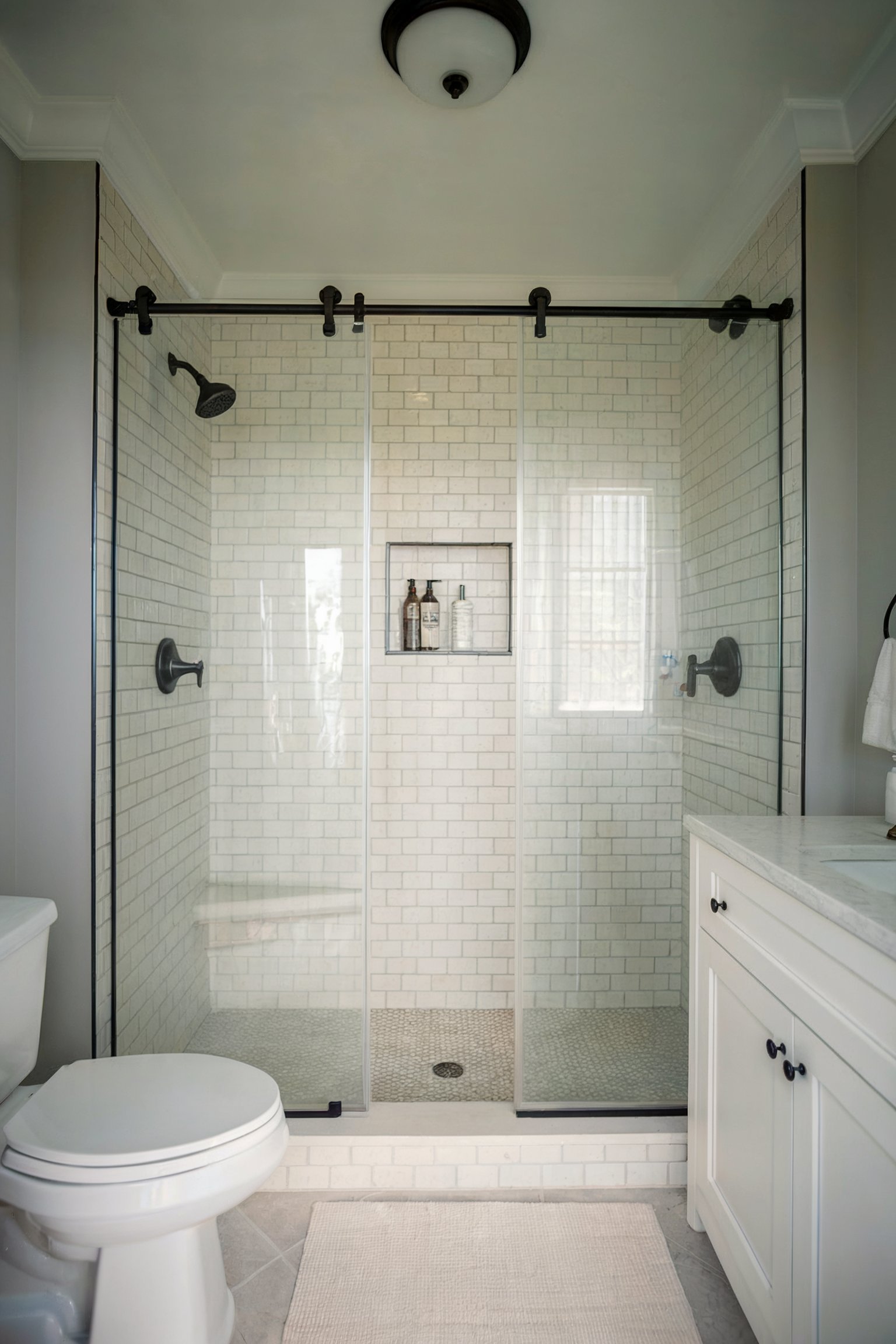 A sleek bathroom with a subway-tiled shower and sliding glass doors, featuring black hardware and a built-in shelf