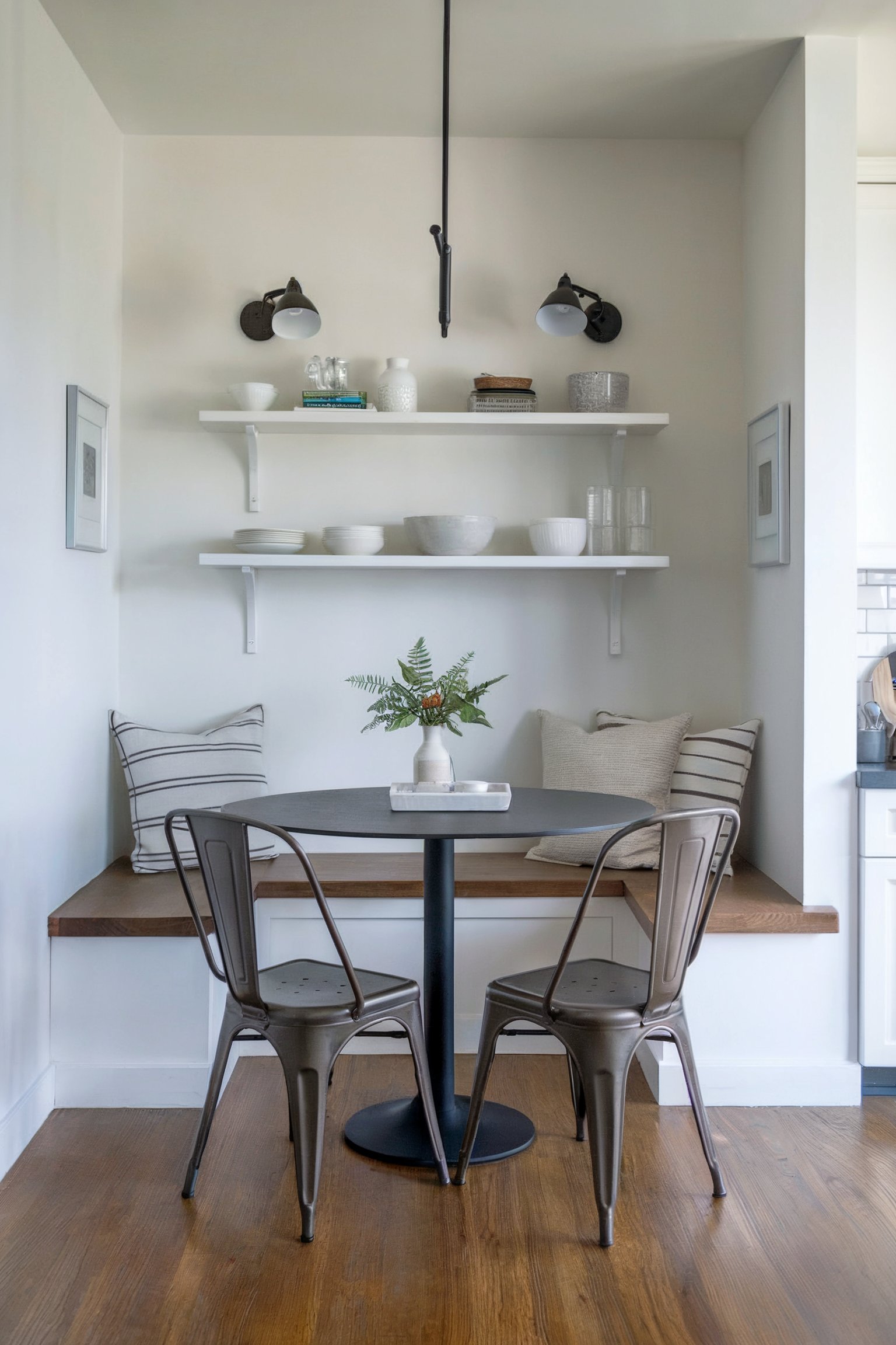 Minimalist nook with metal chairs, bench seating, and white dishware on open shelves