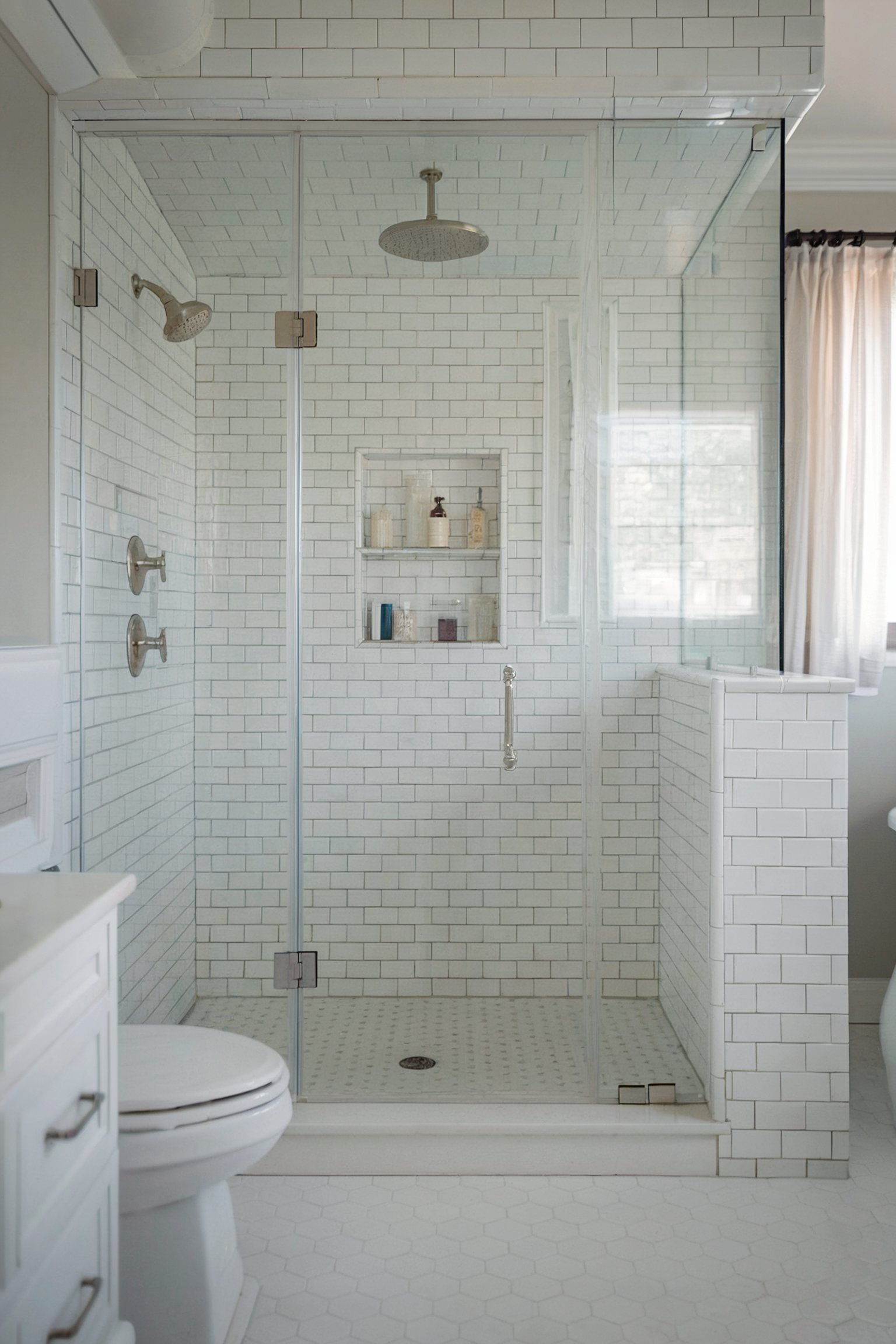 A white, glass-enclosed shower with classic subway tiles and a built-in shelf for shower essentials