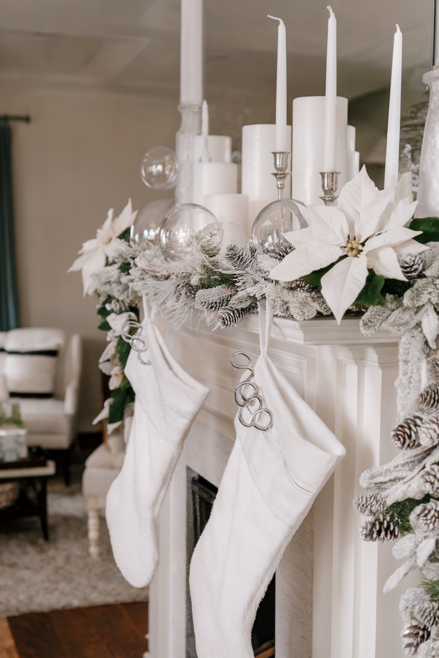 Two white stockings hang on a decorated mantel with candles, poinsettias, pinecones, and ornaments in a festive room