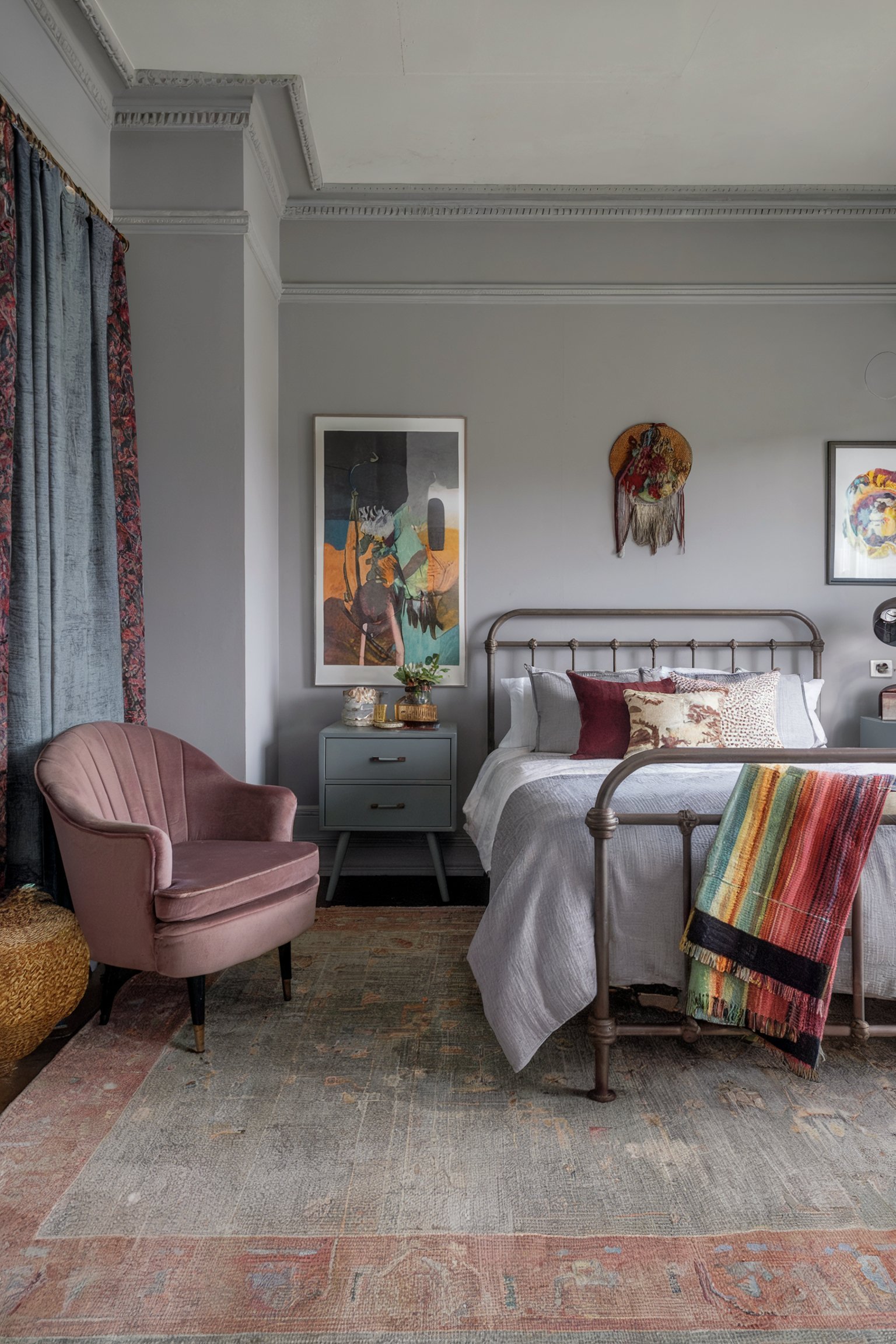 Eclectic bedroom with metal bed frame, colorful throw, blush chair, and unique wall art for a boho feel