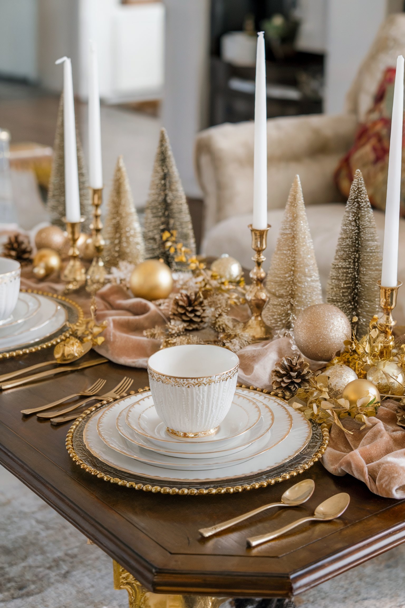 A luxurious holiday table arrangement with gold accents, white candles, pinecones, and golden trees