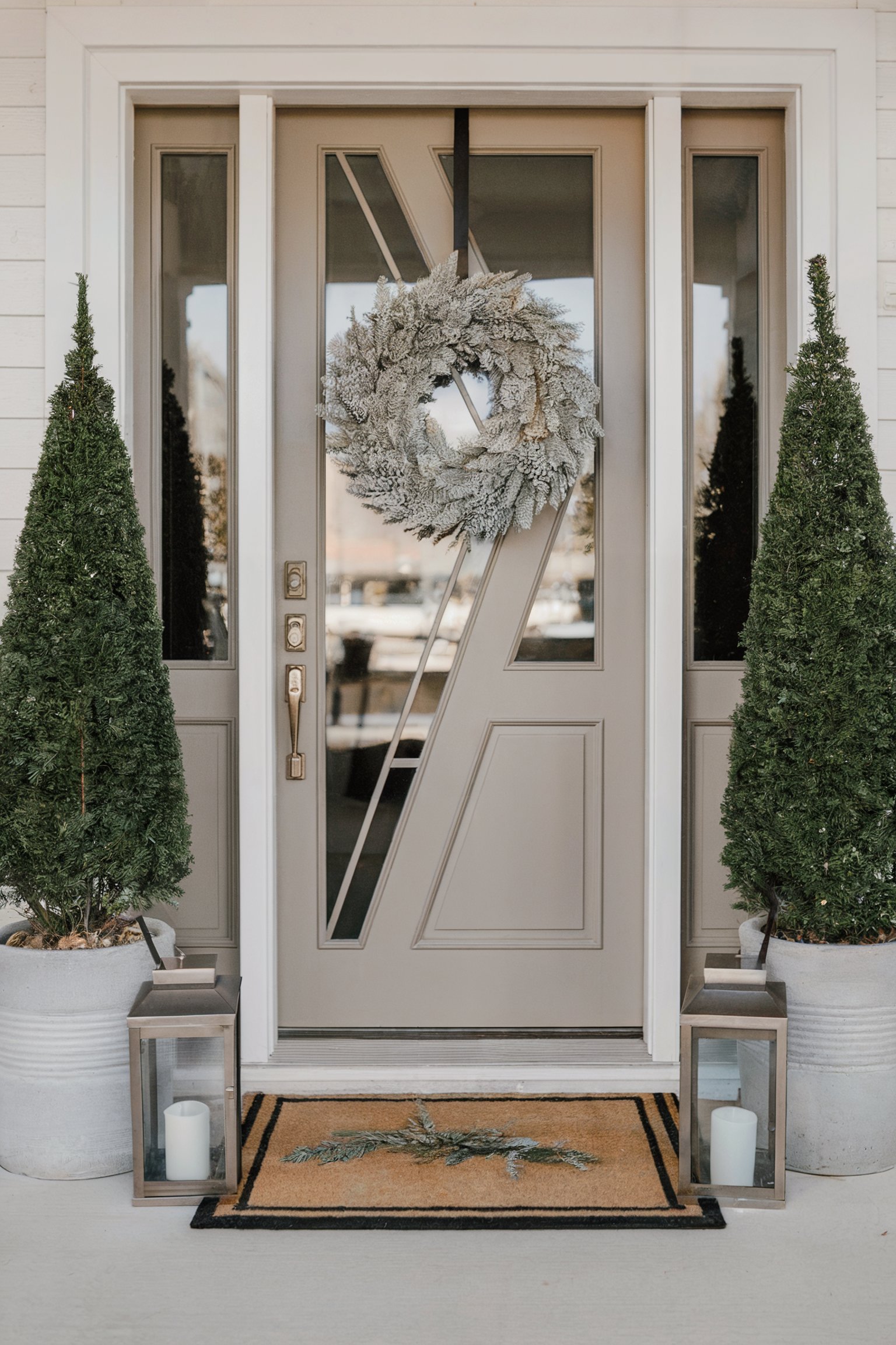 Elegant entrance with a frosted wreath, potted evergreens, and lanterns with candles