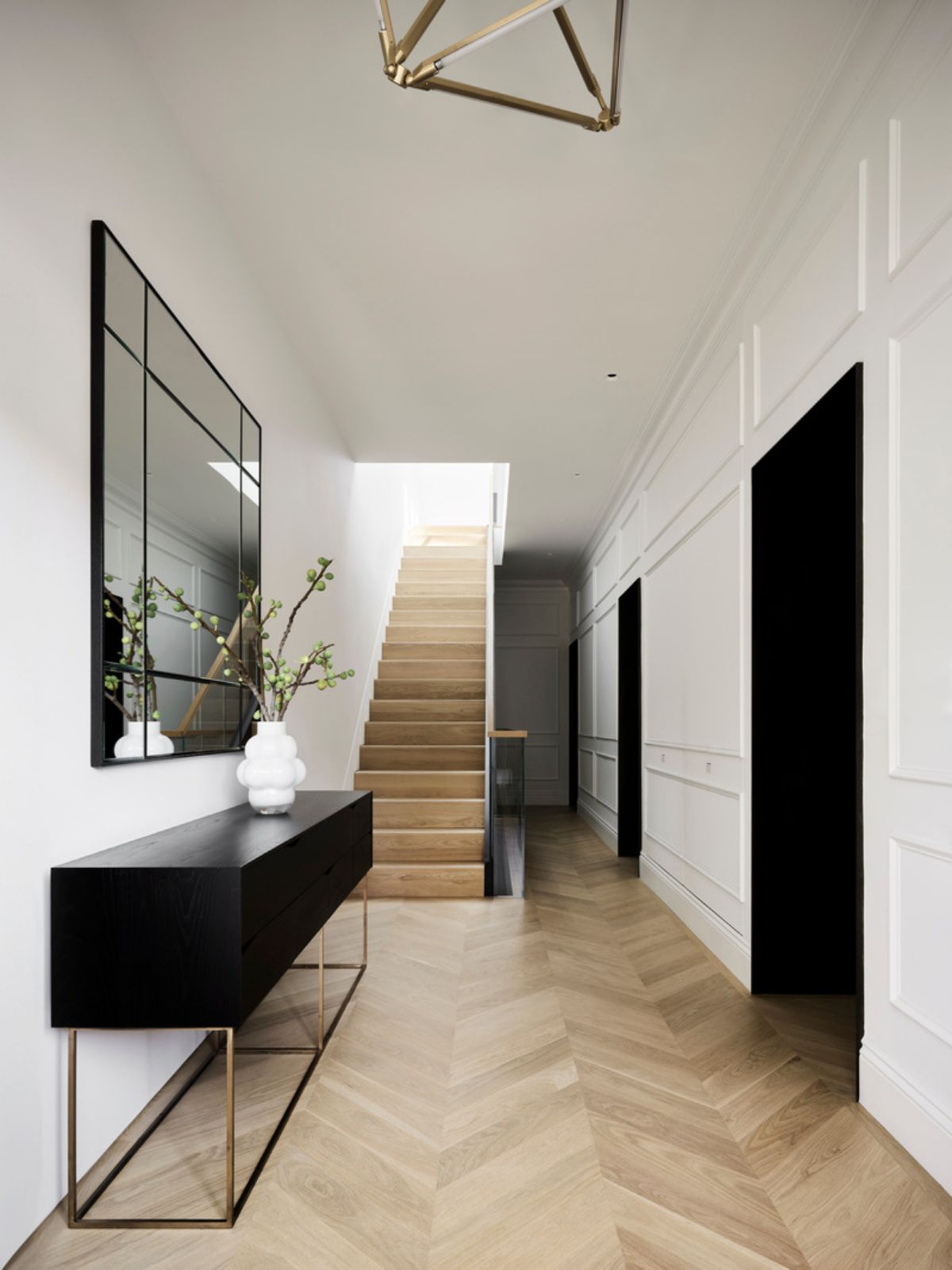 The entry hall features engineered, white oak unfinished 5" wide boards in a chevron pattern. The light fixture, SHY 17 by Bec Brittain, was designed and made in New York City from thin LED tubes and brass.