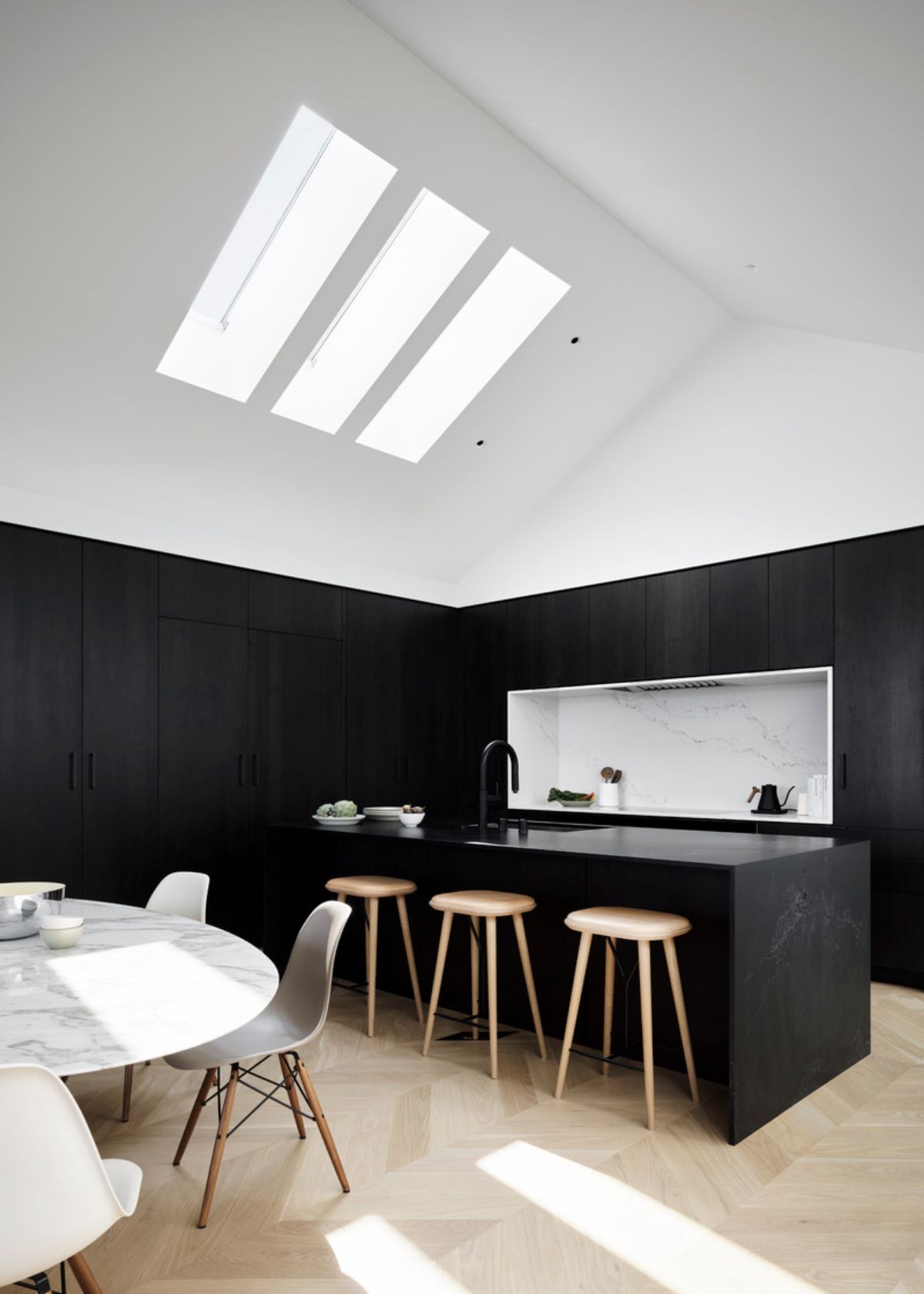 In the kitchen and dining area, black walnut cabinetry by Seattle-based Henrybuilt sits dramatically below the white peaked roof. The Empira Black honed quartz used for the island and the Statuario Nuovo honed quartz which wraps the cooktop are from Caesarstone.