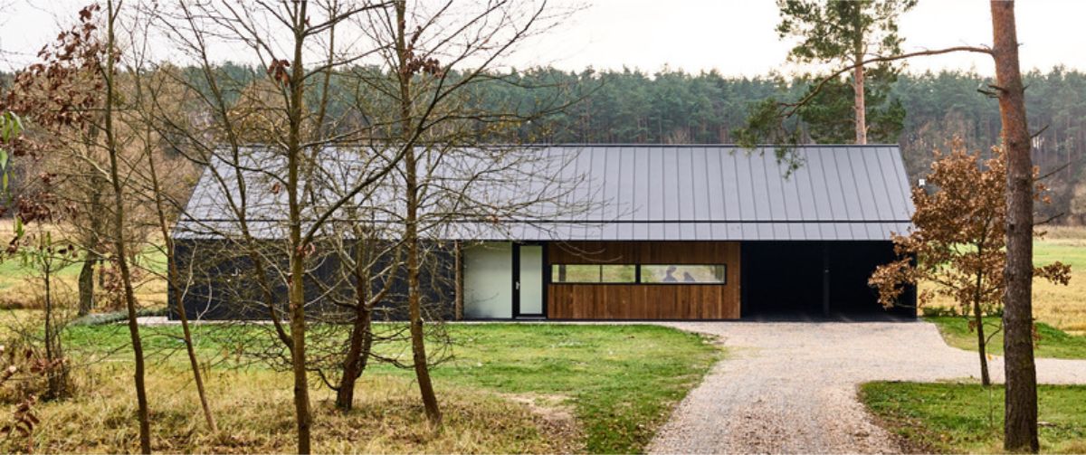 Long, low-slung house situated in wooded area with a dark colored flat roof