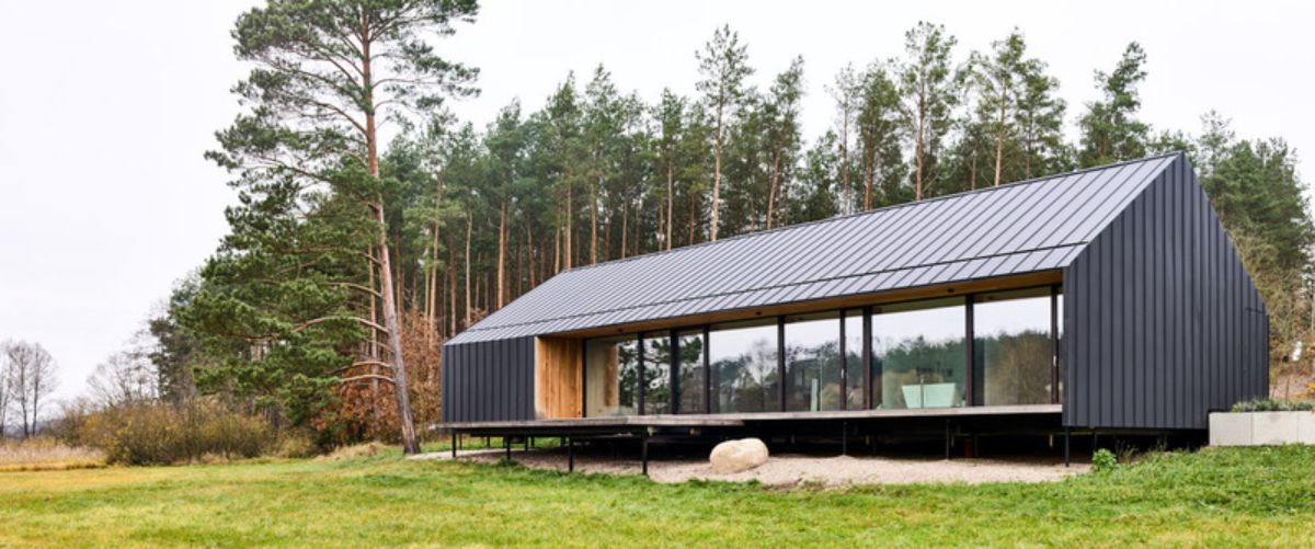 The house is dark-colored with a long low-pitched roof and large windows along one side