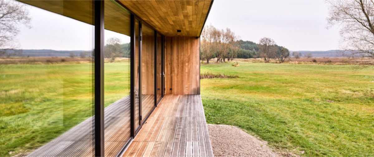 Modern house with floor-to-ceiling windows offering an expansive view of a grassy field and distant trees