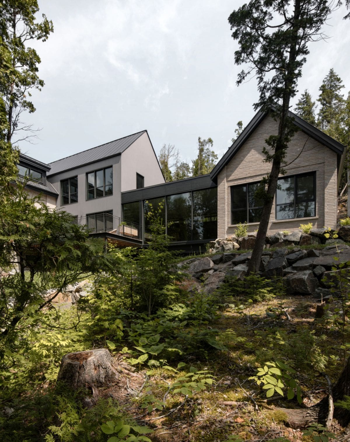 House built on the edge of a sharp sloping terrain descending towards the water's edge, and engulfed by lush nature