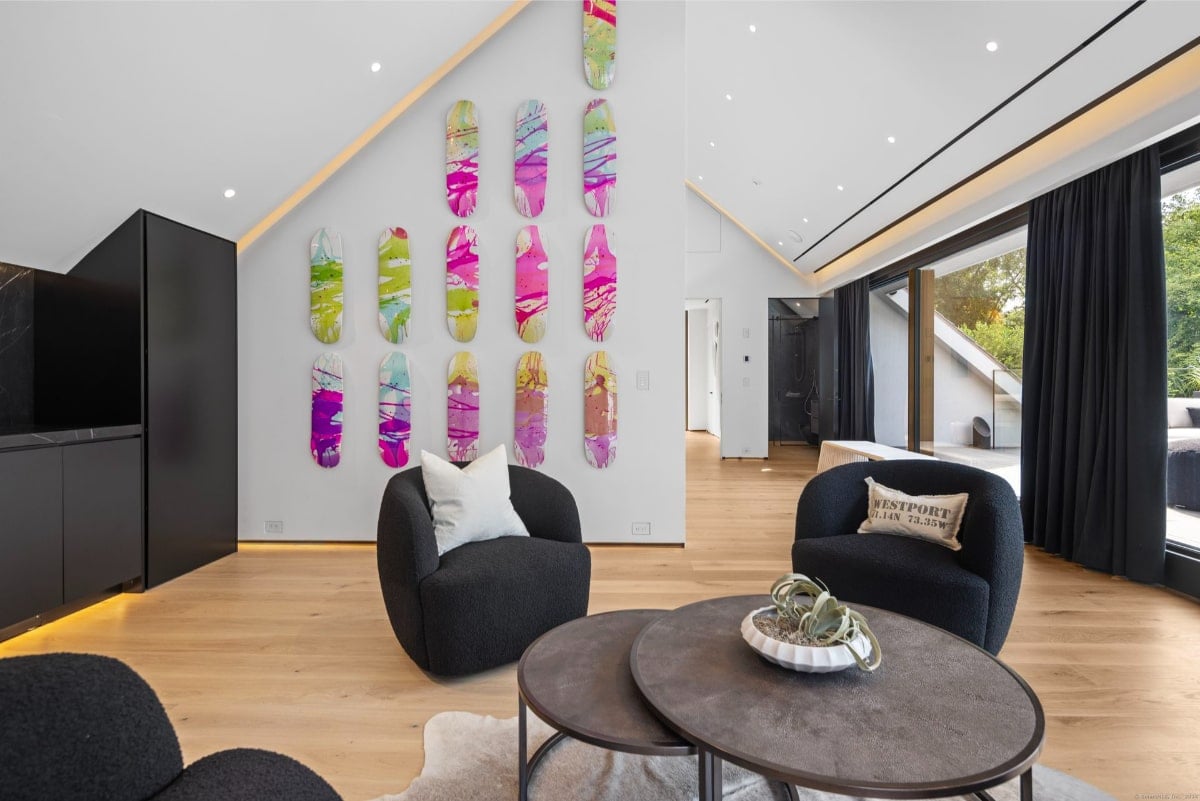 Living space with a unique feature: a wall decorated with a collection of colorful, artfully arranged skateboards. The room is furnished with comfortable, dark-colored armchairs and a low coffee table. The flooring is light-colored wood.