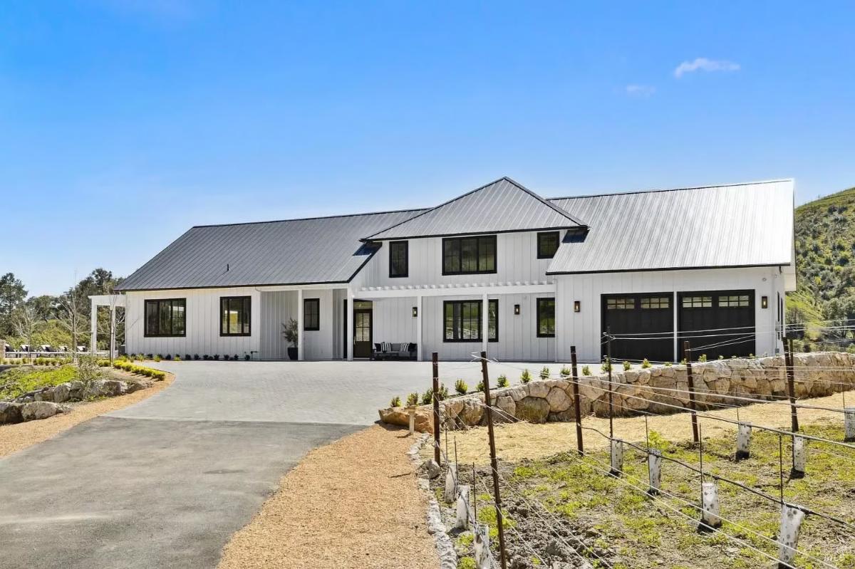 Exterior of a modern white house with a pitched roof, driveway, and surrounding vineyard.