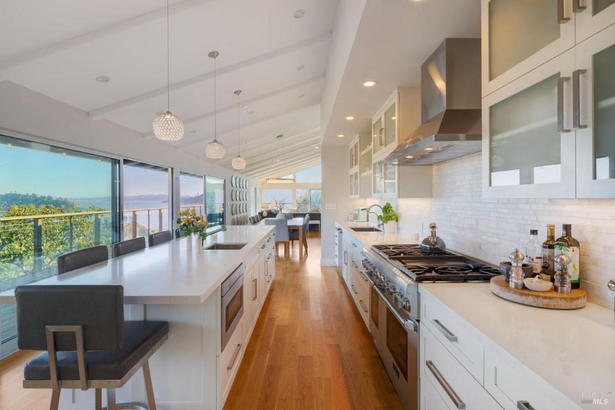 A modern kitchen features a long island, sleek cabinetry, and large windows showcasing a view of the water.
