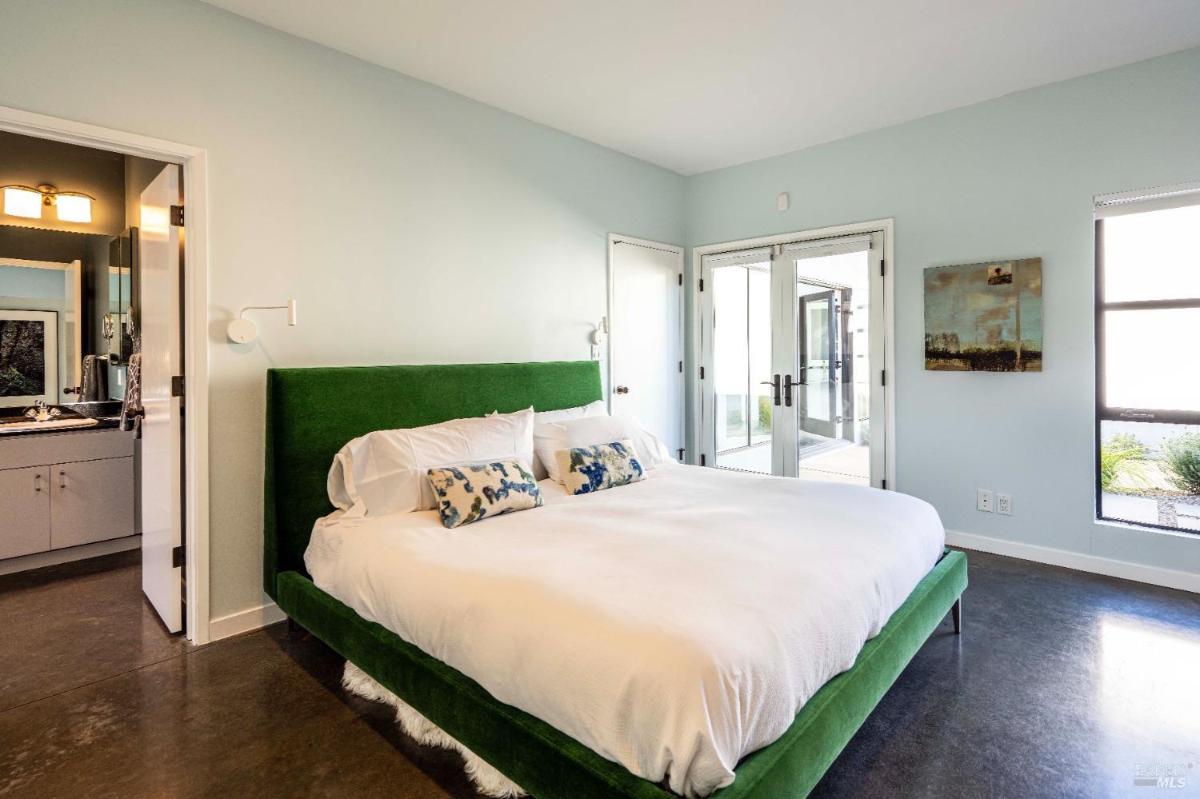 A bedroom featuring a green upholstered bed and access to a patio through glass doors. 