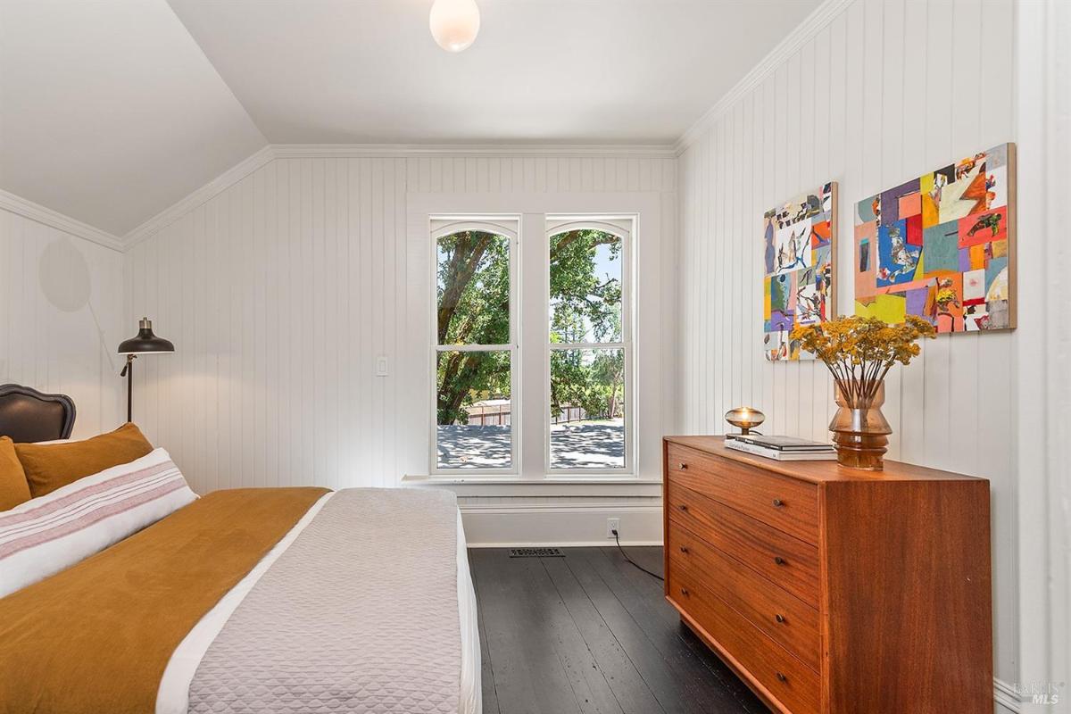 Bedroom with a wooden dresser, bed, and windows with outdoor views.
