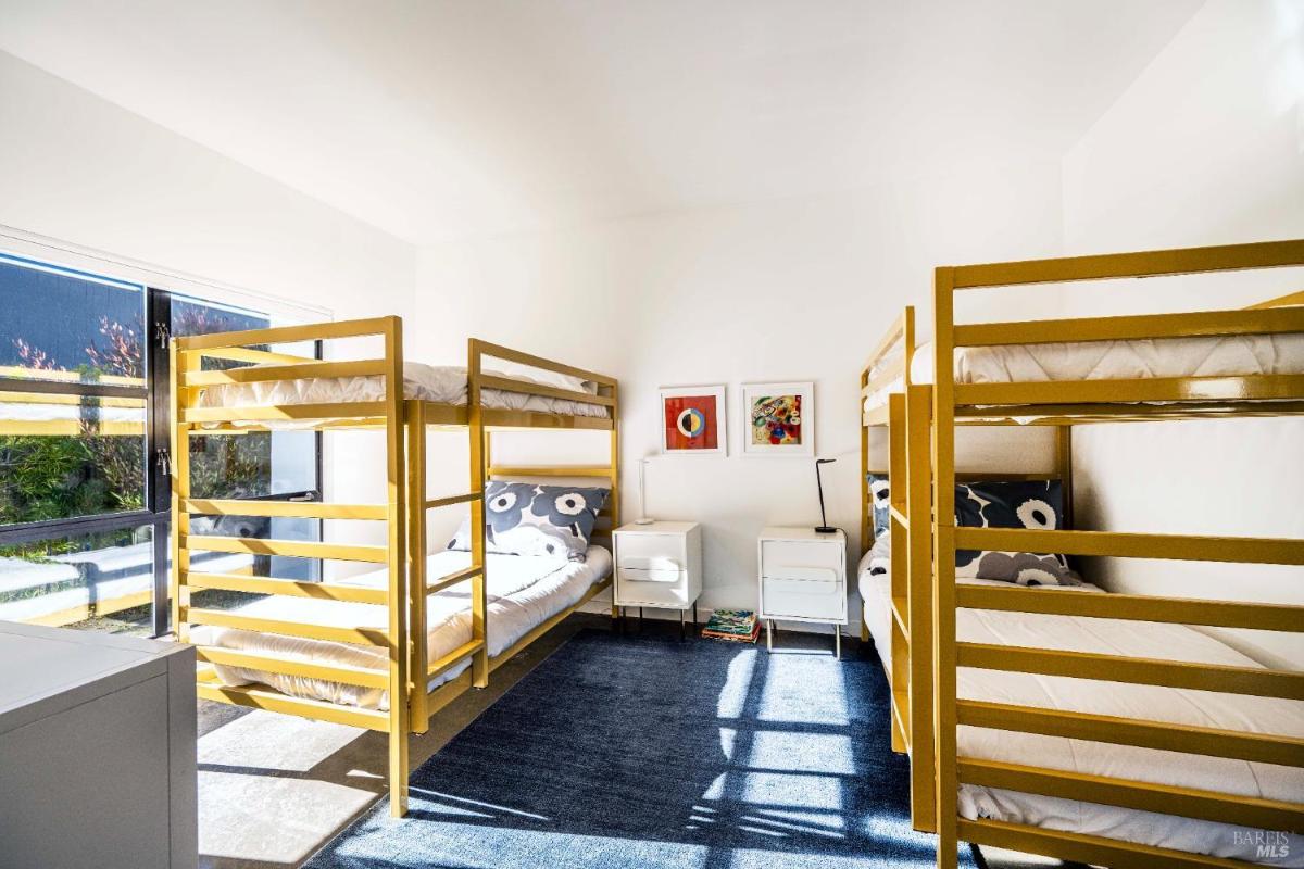 A room with two sets of yellow bunk beds and sunlight coming through large windows. 