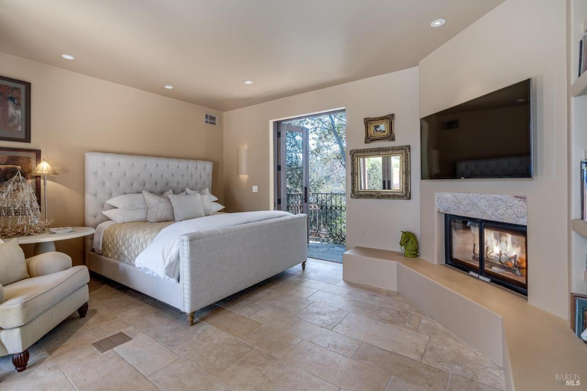 Bedroom with a fireplace, upholstered bed, and access to a balcony.