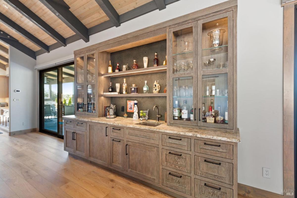 Built-in bar cabinet with glass shelving, storage drawers, and a granite countertop in the living area.