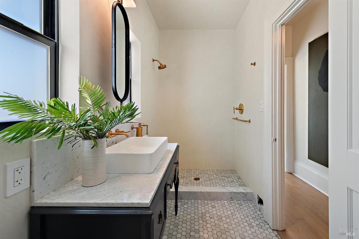 Bathroom with walk-in shower, marble countertop, and decorative mirror.