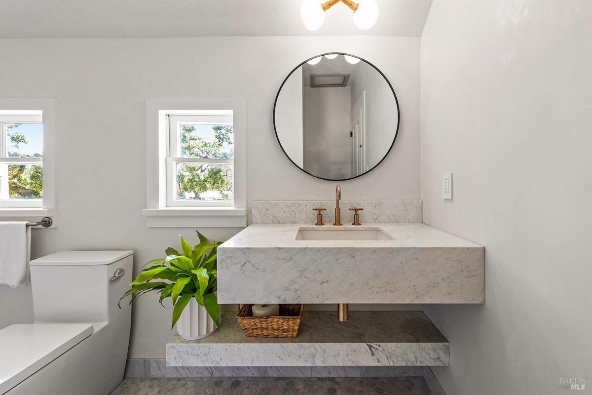 Bathroom with round mirror, marble sink, and windows.