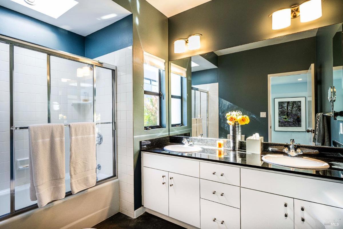 A bathroom design with a glass shower, dual sinks, and large windows allowing natural light. 