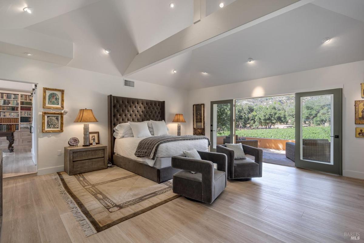 Bedroom with a vaulted ceiling, padded headboard, and seating area.