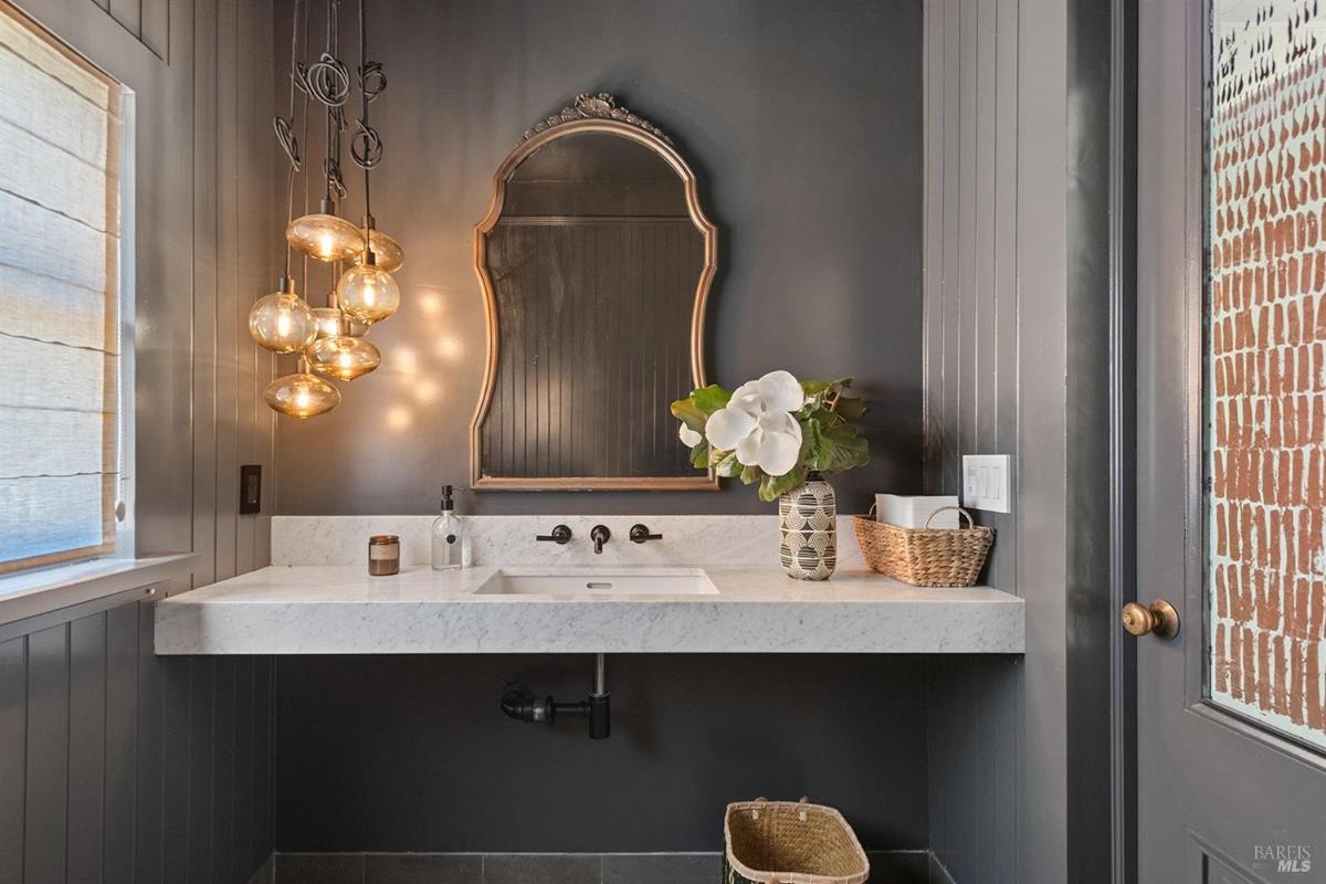 Powder room with dark walls, marble sink, and decorative lighting.