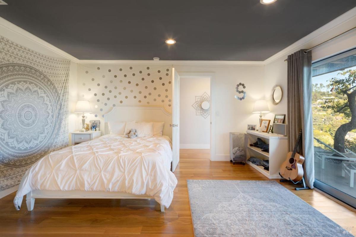 A bedroom with a bed, nightstands, a guitar, a shelf, and sliding glass doors leading outside.