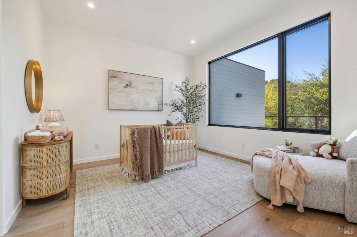 A nursery room with a crib, a chair, and a large window.