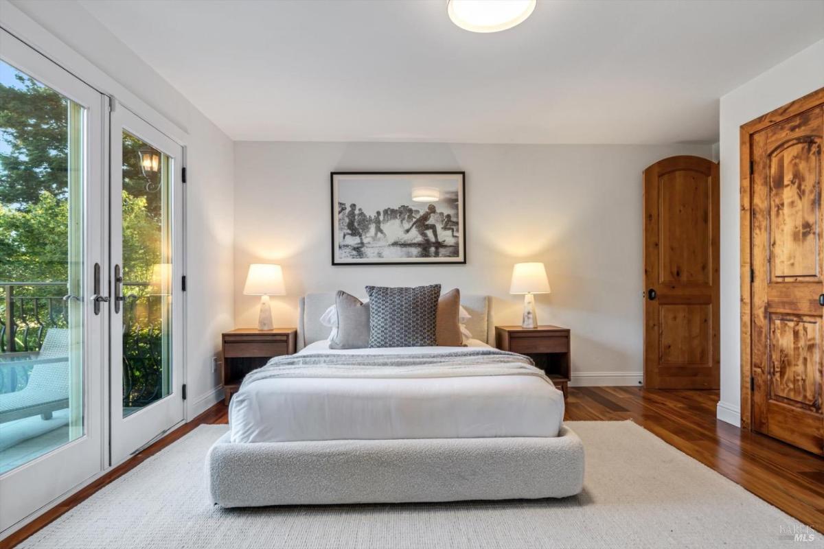 Bedroom with a bed, nightstands, and wooden doors next to a windowed balcony.