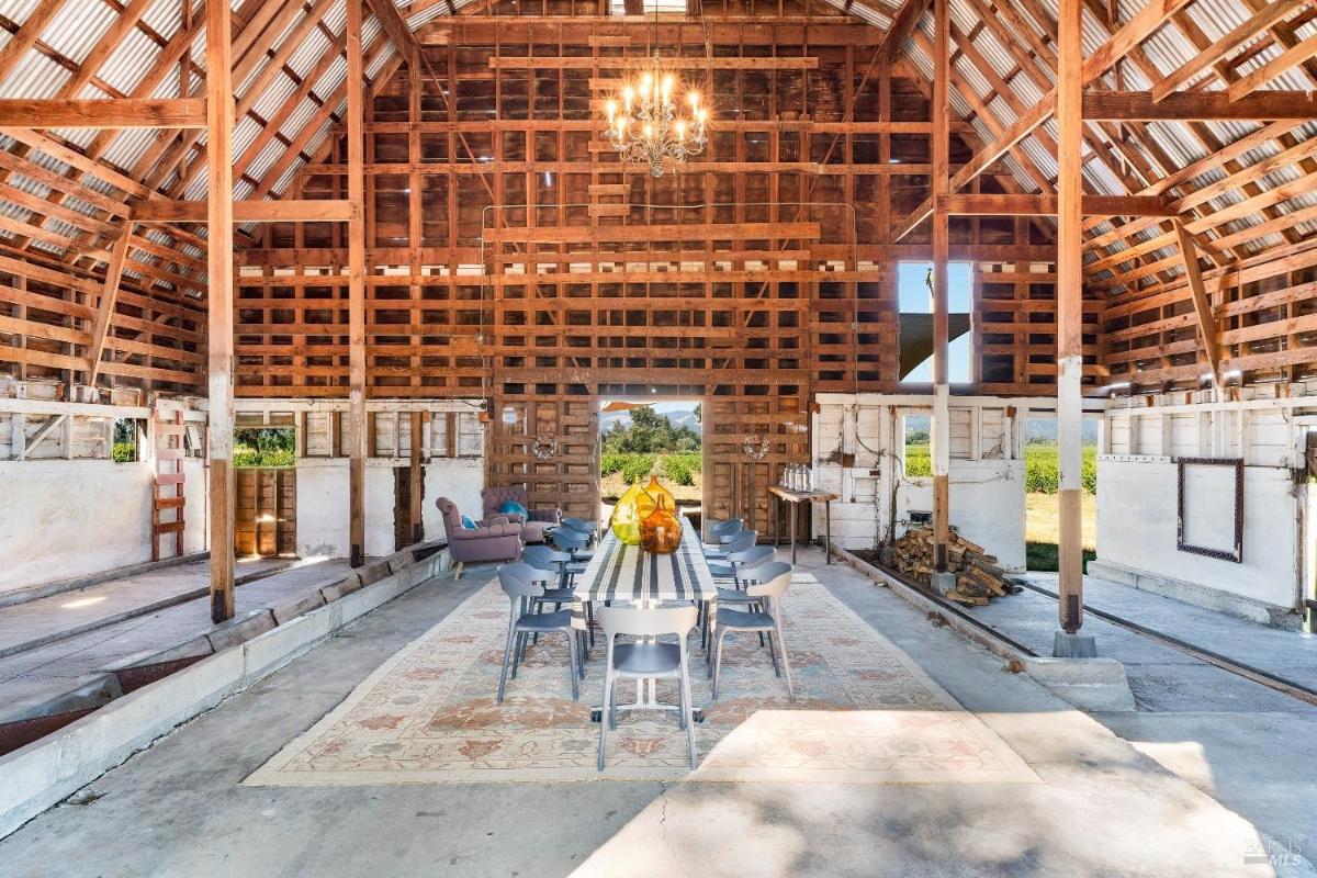 Barn interior with wooden beams, dining table, and chandelier.