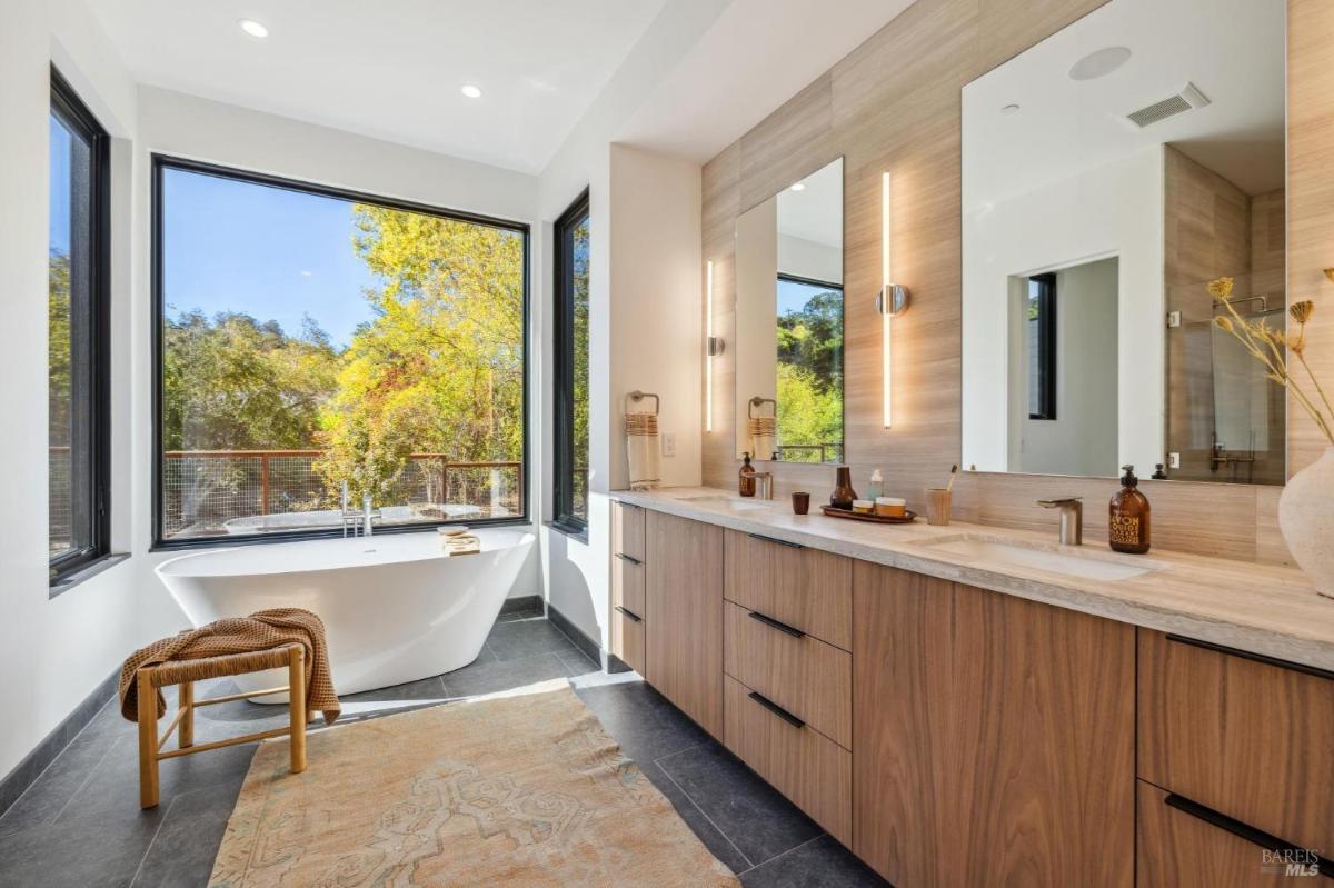 A bathroom with a freestanding tub, dual sinks, and large windows.