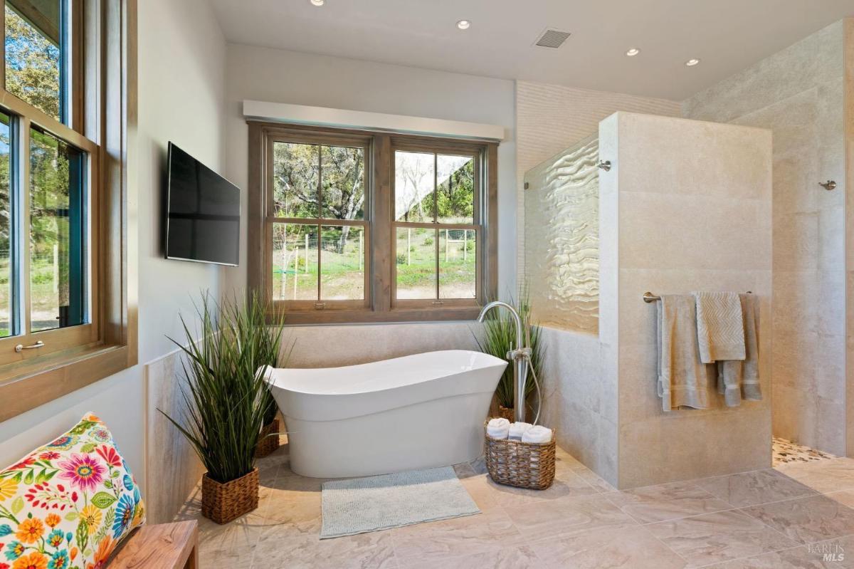 A bathroom with big freestanding tub, potted plants, and picture windows.