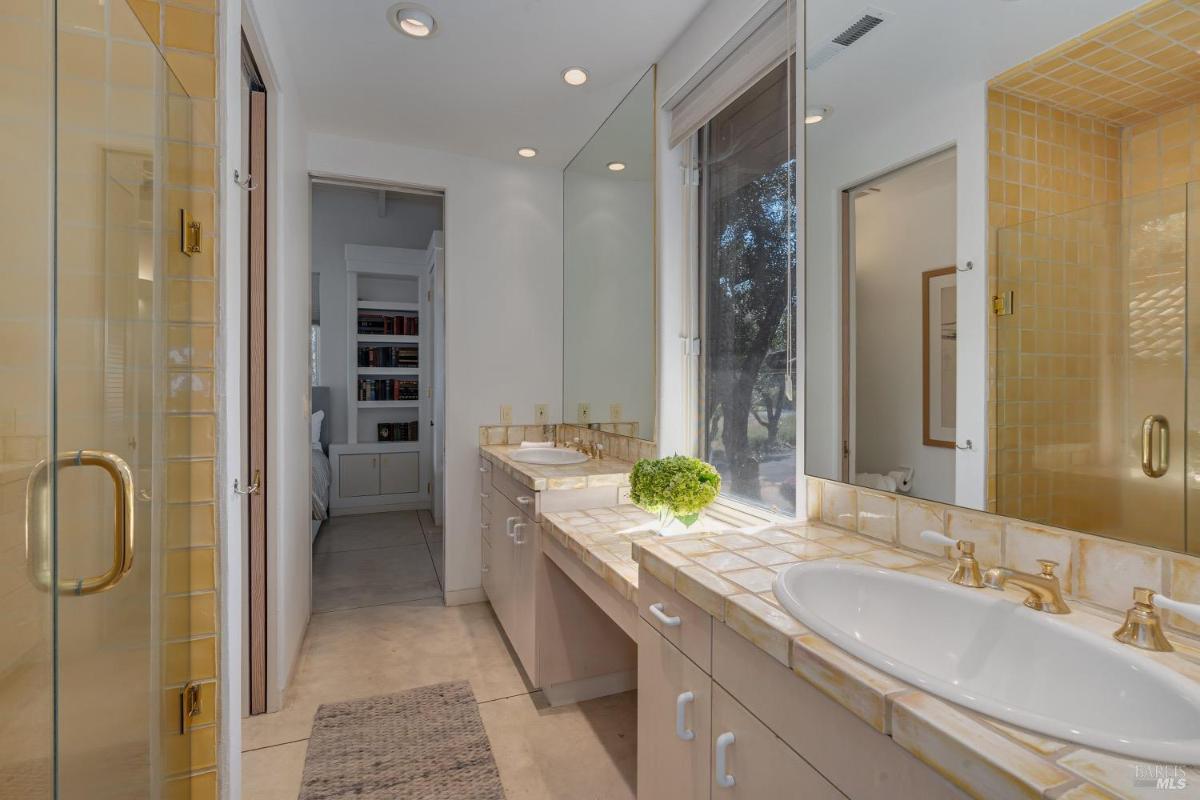 Bathroom with a tiled countertop, dual sinks, and a shower.