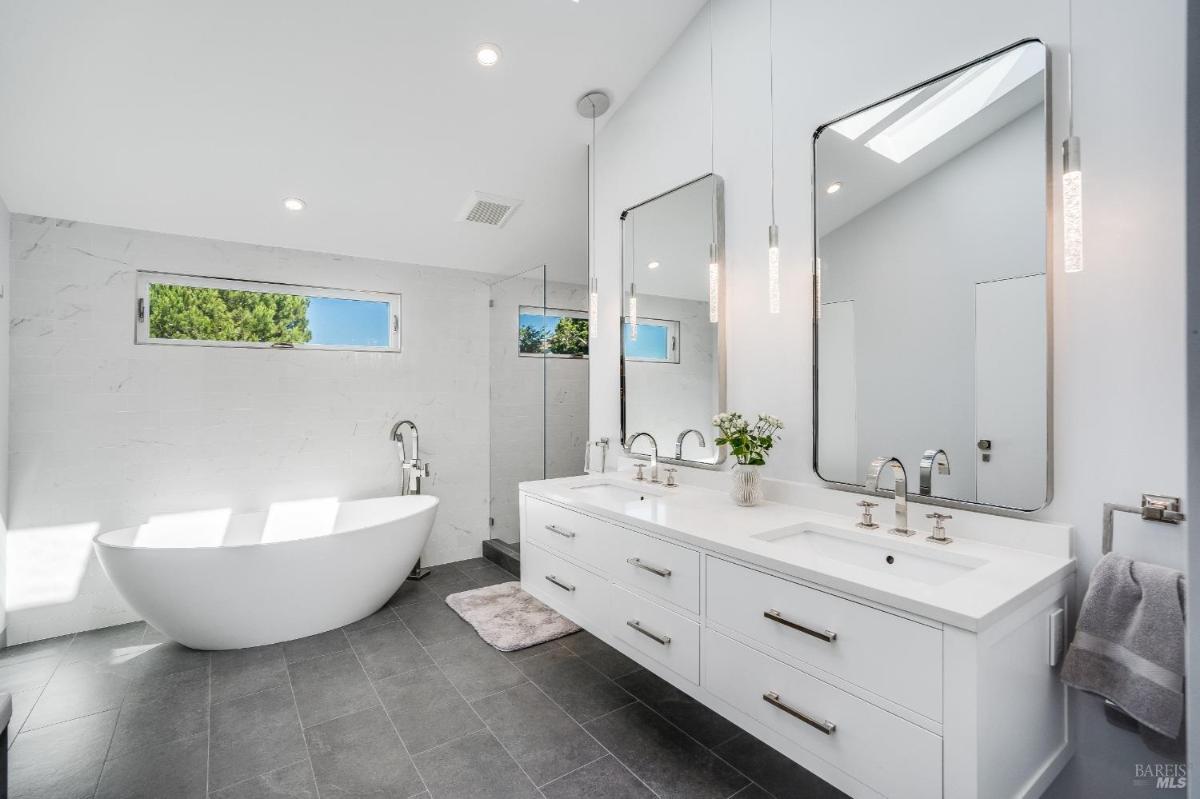 A bathroom with a freestanding bathtub, double vanity, large mirrors, and a glass-enclosed shower.