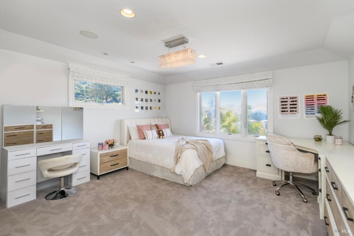 Bedroom with a queen-sized bed, vanity, desk, and large windows offering a view of greenery.
